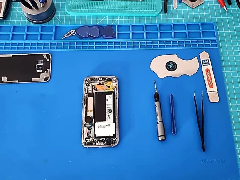 Aufgeklapptes iPhone auf blauer Reparaturmatte mit professionellen Werkzeugen und Komponenten